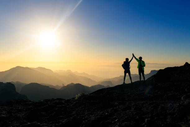Couple hikers celebrating success concept in mountains Couple hikers celebrating success in sunset mountains, accomplish with arms up outstretched. Young man and woman on rocky mountain range looking at beautiful inspirational landscape view, Gran Canaria Canary Islands. high section photos stock pictures, royalty-free photos & images