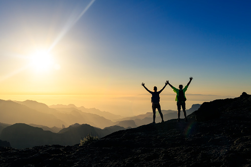 Couple hikers success and trust in mountains, accomplish with arms up outstretched. Young man and woman looking at beautiful inspirational landscape view, Gran Canaria Canary Islands.
