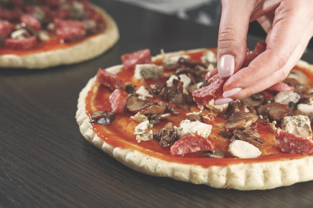 pizza cooking, meat of chiken, sausage salami, thick dough,  pizza crust, chef prepares delicious pizza, pizza with chicken and sausage salami, cooking process, hand of woman, mushrooms,  champignon - pizza sauces chef making imagens e fotografias de stock