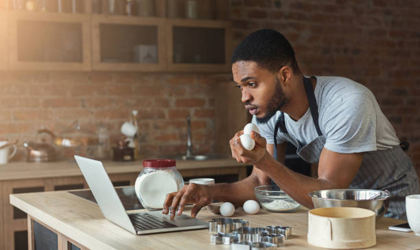 istock Black man baking pastry and looking recipe in laptop 1069988958