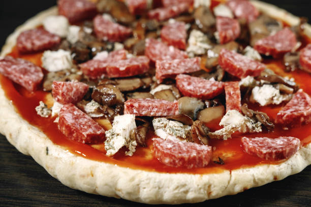 pizza cooking, meat of chiken, sausage salami, thick dough,  pizza crust, pizza is on a dark table, pizza with chicken and sausage salami, cooking process, mushrooms,  champignon - pizza sauces chef making imagens e fotografias de stock