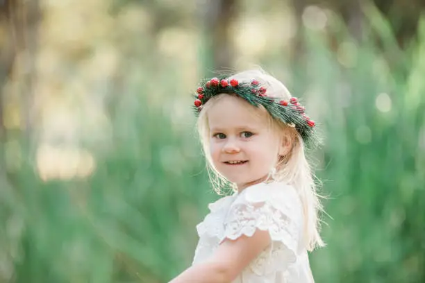 Young blonde girl celebrating a summer Christmas outdoors wearing white and red festive colours and a holly berry wreath flower crown