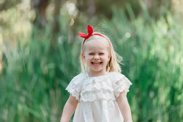 Little girl with blonde white hair smiling at the park wearing a red bow in her hair