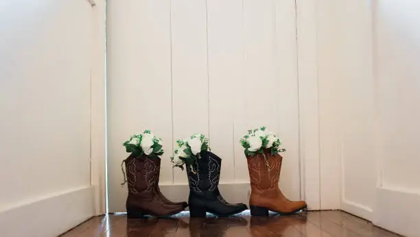 Leather cowboy cowgirl boots with flower bouquet for bride and bridesmaids on wedding day. Rustic country barn wedding.