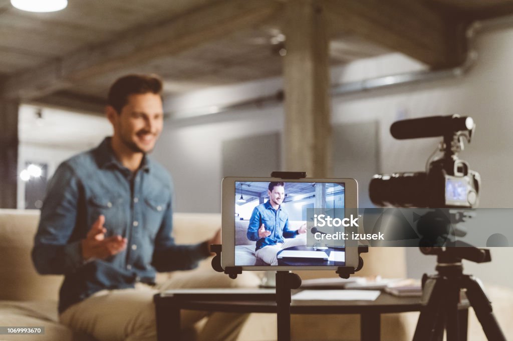 Male vlogger recording content on camera Young man talking in front of camera. Male vlogger recording content on camera and digital tablet. Home Video Camera Stock Photo