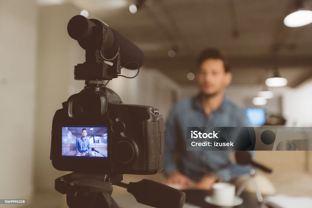 Man making video blog Young man talking in front of camera. Male vlogger recording content on camera, focus on camera display screen. Home Video Camera Stock Photo