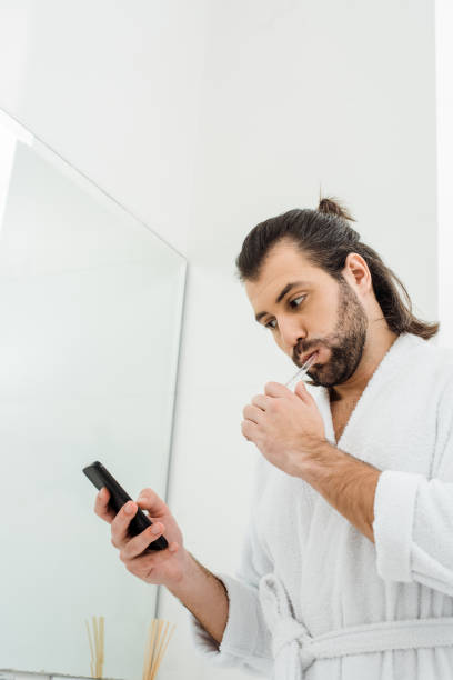 istock handsome adult man brushing teeth and using smartphone in morning 1070002070