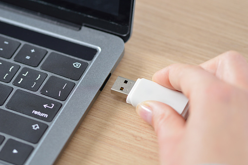 Close up of a woman hand connecting a pendrive in a laptop on a desktop