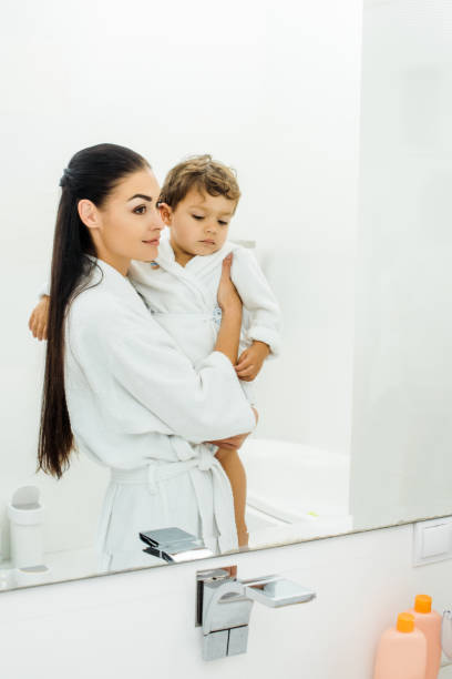 istock beautiful mother holding son in white bathrobe in bathroom 1070011832