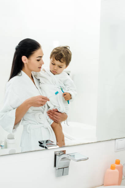 istock mother and son in white bathrobes brushing teeth together 1070011842