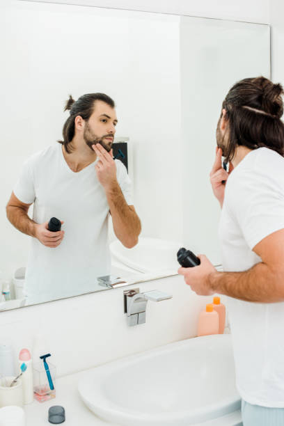 istock Handsome man holding shaving foam and looking in mirror in bathroom 1070012268