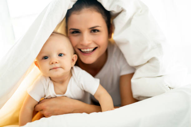 retrato de uma jovem mãe com bebê infantil menina liying na cama coberta com um manto branco - family with one child domestic life caucasian love - fotografias e filmes do acervo