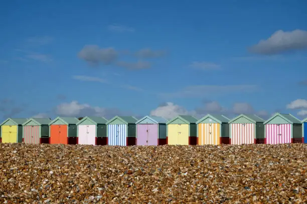 Photo of a line of colorful brighton beach huts on a pebble beach with blue sky