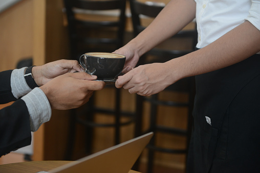 A barista serves a cup of coffee to an Asian businessman in a cafe