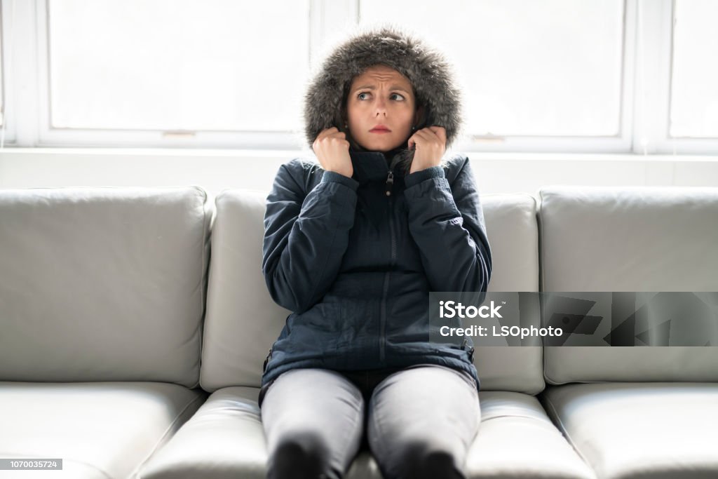 Woman have cold on the sofa at home with winter coat A woman have cold on the sofa at home with winter coat Cold Temperature Stock Photo