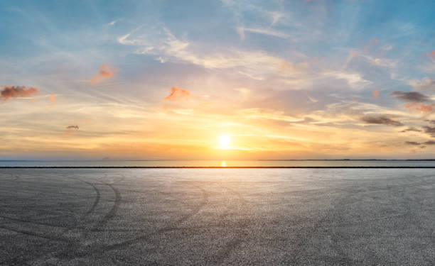 アスファルト舗装と海岸線の劇的な空 - sunset dusk ストックフォトと画像