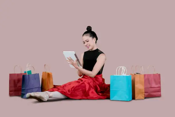 Young ballerina using a digital tablet for shopping online while sitting near paper bags in the studio