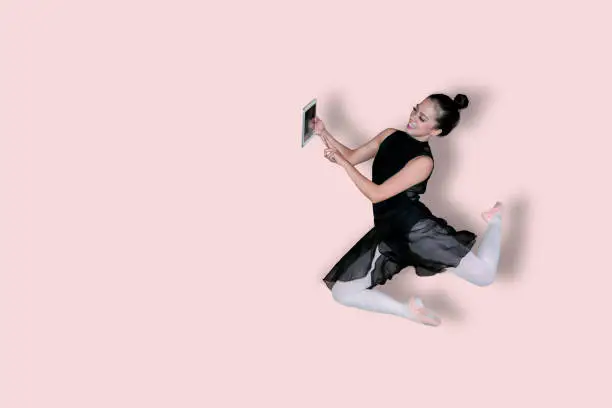 Picture of young female ballerina holding a digital tablet while dancing in the studio
