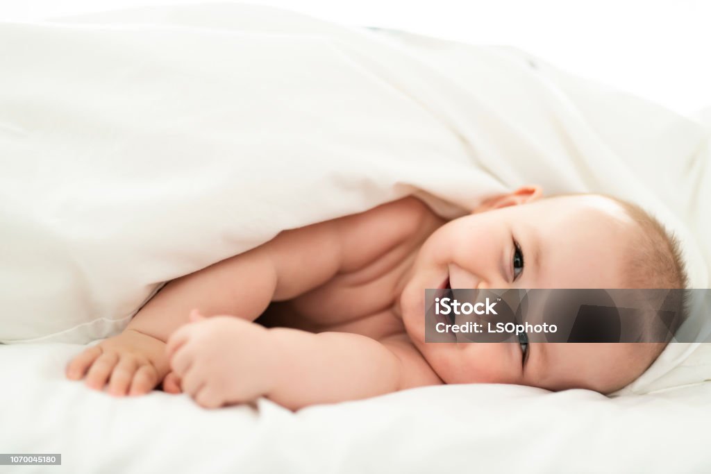 happy cute baby lying on white sheet A happy baby lying on white sheet Baby - Human Age Stock Photo