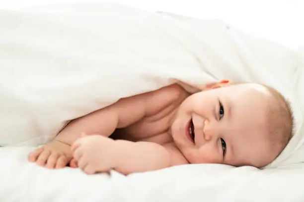 Photo of happy cute baby lying on white sheet
