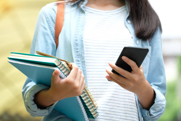 istock Student girl holding books and using smartphone, online education, technology communication 1070046010