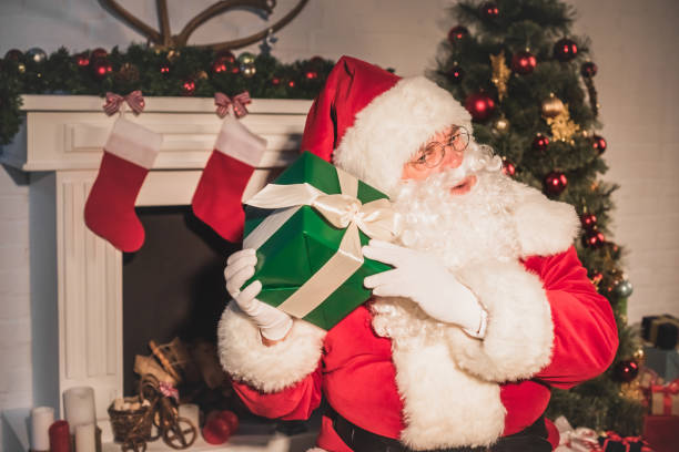 istock santa claus holding and shaking christmas gift while sitting near fireplace 1070052982