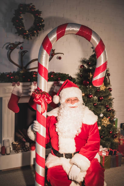 istock santa holding big candy cane and looking at camera near fireplace 1070053822
