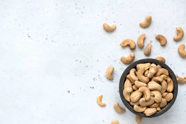 Cashew nuts in bowl on grey concrete background with copy space for text. Top view, healthy vegetarian food