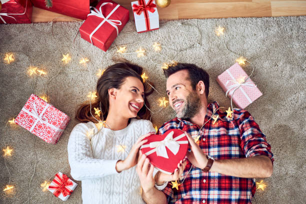 Portrait of cute couple holding presents together in room with Christmas decorations stock photo