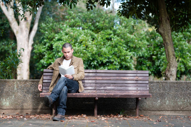 Man reading a book in a park bench