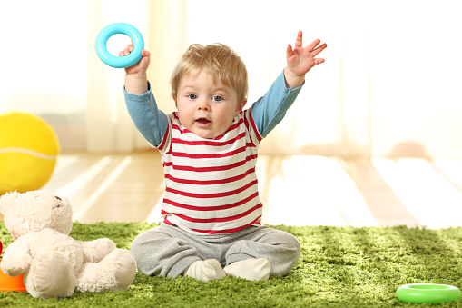 Happy baby raising arms with a toy on a carpet on the floor at home