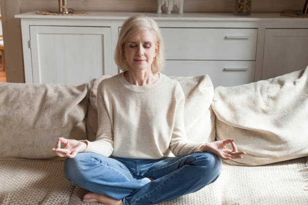 istock Calm senior woman practicing yoga meditating on couch 1070069624