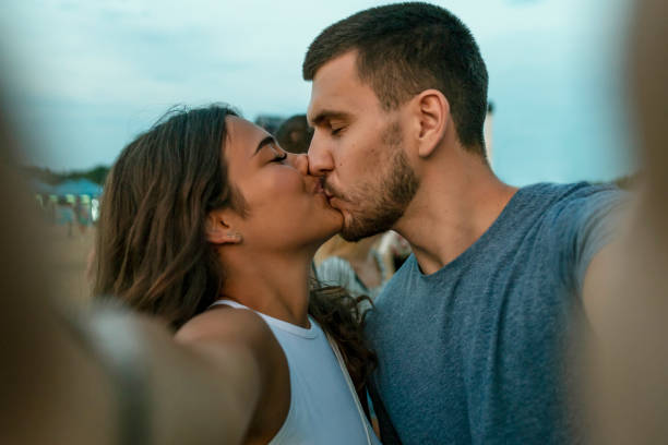 Capturing Bright Moments. Joyful Young Loving Couple Making Selfie on Camera While Standing Outdoors. Happy Smiling Couple Kissing and Taking Selfie Photo