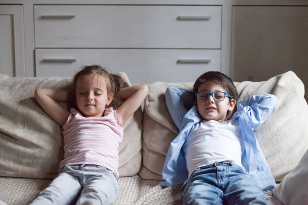 Little preschool girl and boy relaxing sitting on couch Silent preschool sister and brother sitting on sofa in living room at home. Siblings closing eyes have break breath fresh air putting hands behind heads relaxing thinking. Weekend daydreaming concept mindfulness kids stock pictures, royalty-free photos & images