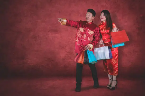 Chinese New Year Concept. Young Asian man pointing something in the studio after buying gifts with his wife