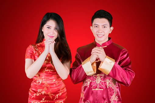 Picture of young Chinese couple smiling at the camera while congratulating Chinese new year in red background