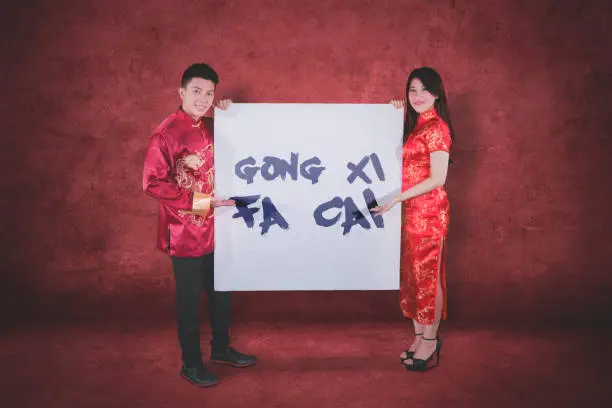 Picture of happy couple wearing cheongsam clothes while showing text of Gong Xi Fa Cai on a whiteboard