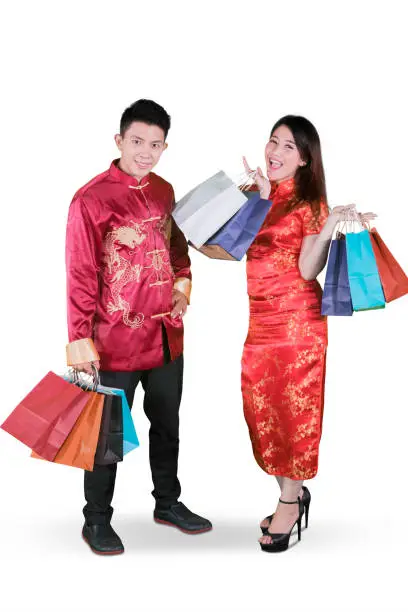 Chinese New Year Concept. Happy young couple wearing traditional cheongsam clothes while holding shopping bags in the studio