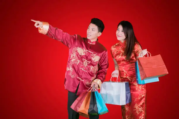 Chinese New Year Concept. Two people holding shopping bags while pointing at something in red background