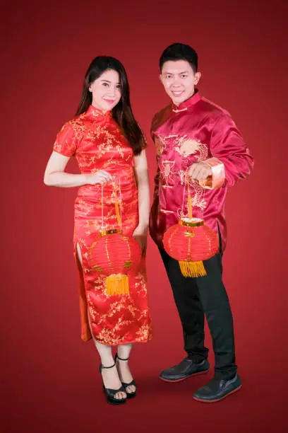 Portrait of a young Asian couple holding lantern at Chinese new year while standing in red background
