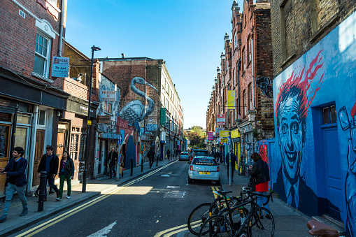 London, UK - 24 October, 2018: wide angle view of people walking on Brick Lane in east London, UK. It is a famous street known for its curry houses and restaurants, and for its Indian and Bangladeshi population. We can see lots of signs, some in neon lights, advertising the many restaurants and markets along the street. Room for copy space.