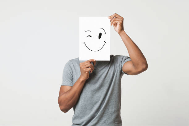 Black man holding paper with smiley face Black man cover his face with happy and winking smiley drawn on paper, white studio background unidentifiable persons stock pictures, royalty-free photos & images