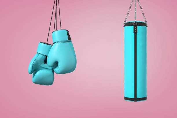 3d rendering of large pair of blue boxing mitts hangs near a blue boxing bag on a pink background. 3d rendering of large pair of blue boxing mitts hangs near a blue boxing bag on a pink background. Sport and recreation. Martial arts. Fighting club. boxing gym stock pictures, royalty-free photos & images