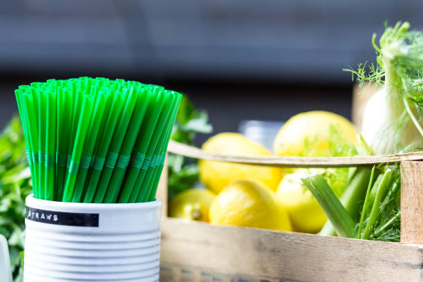 Close up color image depicting a jar of bright green plastic drinking straws on the bar counter of an organic juice bar in London, UK. In the background, defocused, is a selection of lemon and lime citrus fruit. Room for copy space.