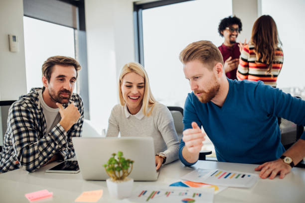 istock Smiling woman using laptop with coworkers 1070122906