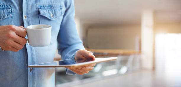 Male hands holding white digital tablet and cup of coffee