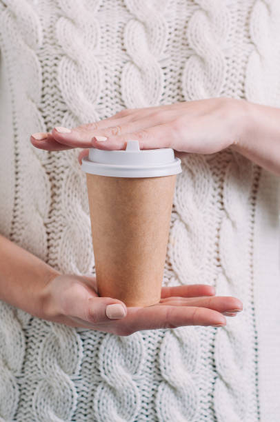 A woman in a white sweater holding a paper Cup of coffee. Template for text or design