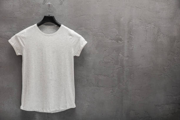 Front side of female grey melange cotton t-shirt on a hanger and a concrete wall in the background stock photo