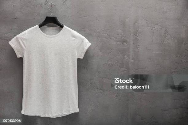 Front Side Of Female Grey Melange Cotton Tshirt On A Hanger And A Concrete Wall In The Background Stock Photo - Download Image Now