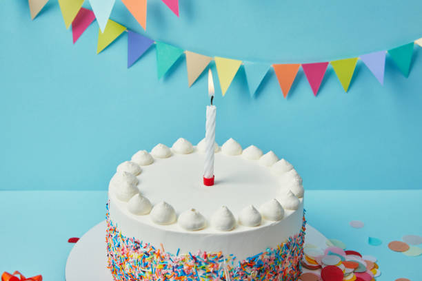 istock Candle on birthday cake with sugar sprinkles on blue background with bunting 1070141914